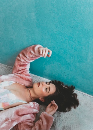 Harper lying down on turquoise colour-block painted concrete in a pink fluffy jacket